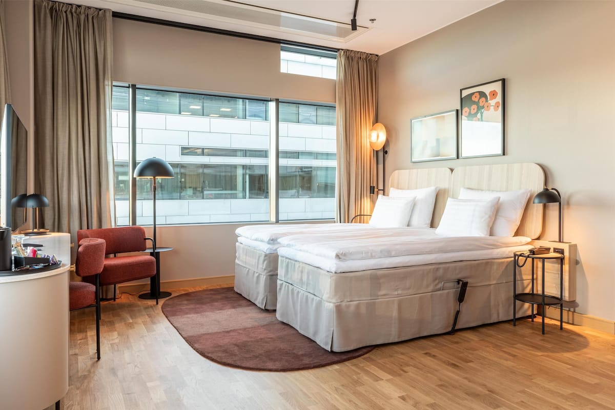 A hotel room with a large bed, a desk, a chair, a small table, and a window with curtains.