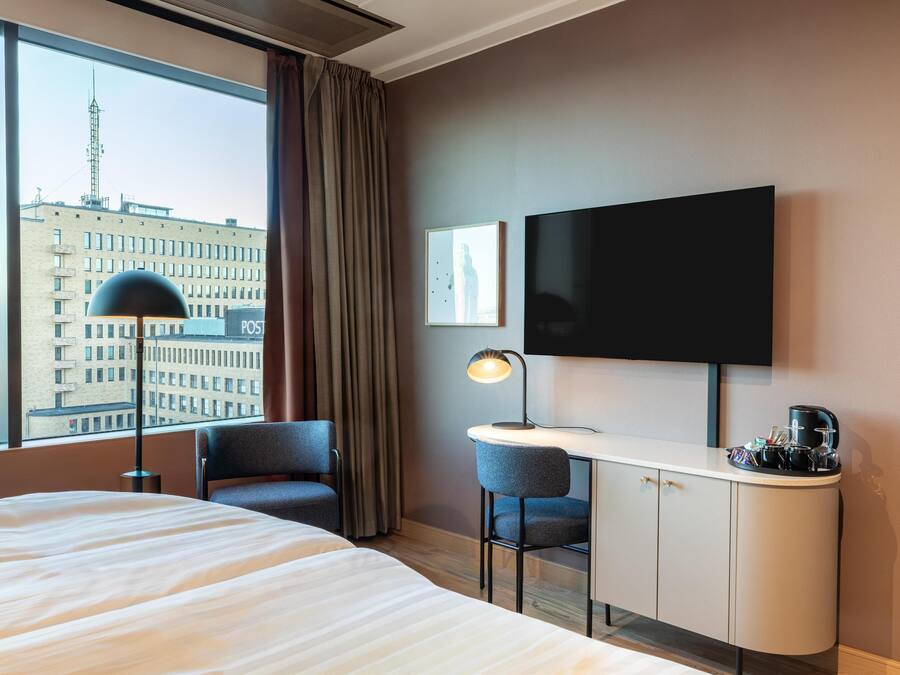 Ein Hotelzimmer mit Bett, Schreibtisch, Stühlen, Fernseher und Blick auf die Stadt.