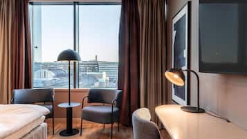 Hotellihuone, jossa on suuri ikkuna, sänky, kaksi tuolia, pieni pöytä ja työpöytä, jossa on lamppu.