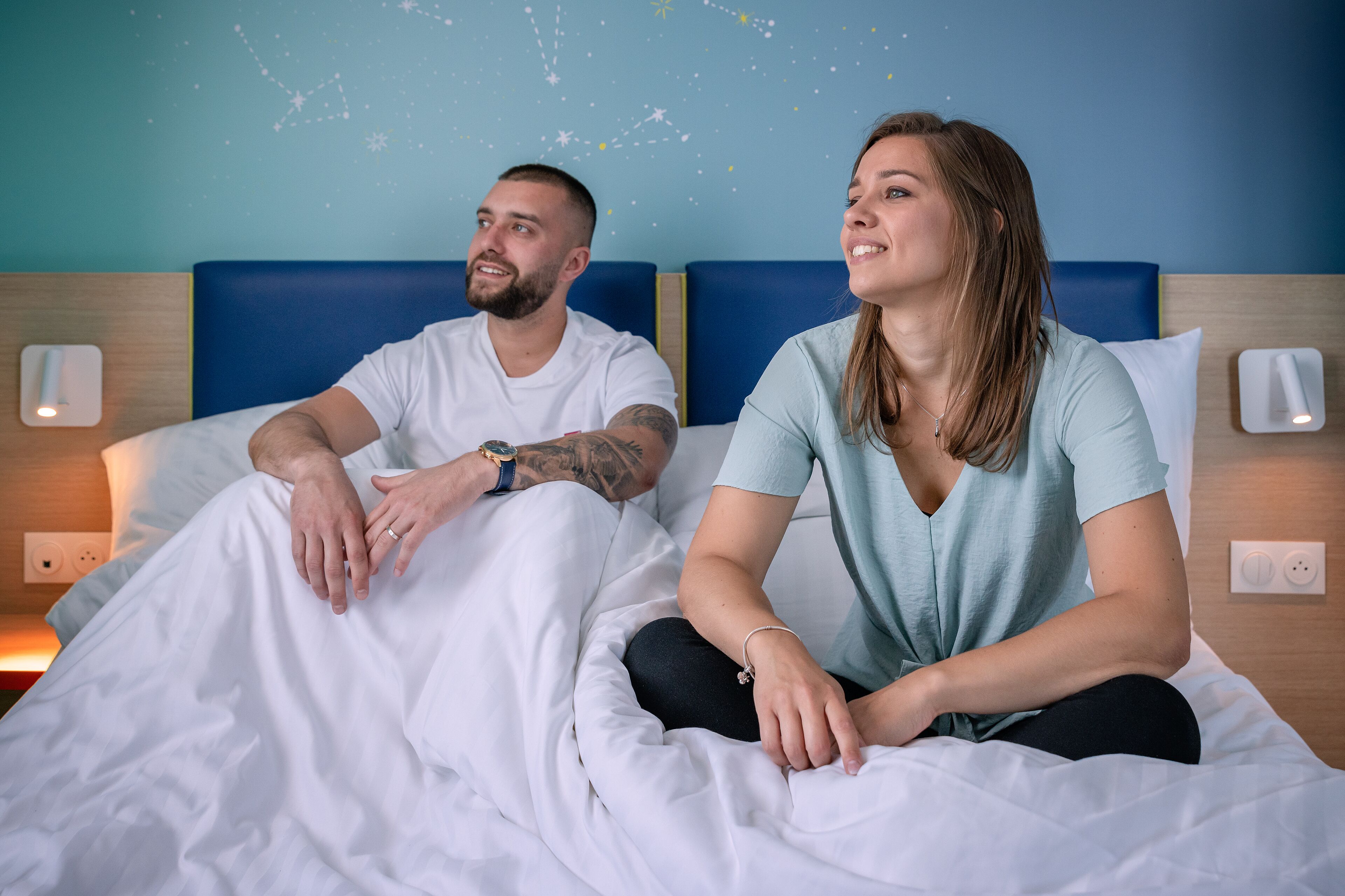 A bedroom with a bed, two pillows, a nightstand, and a wall with a starry design.