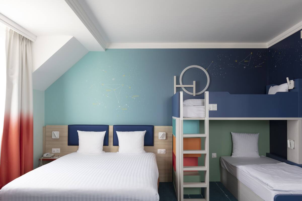 A hotel room with a large bed, a bunk bed, a desk, and a nightstand.