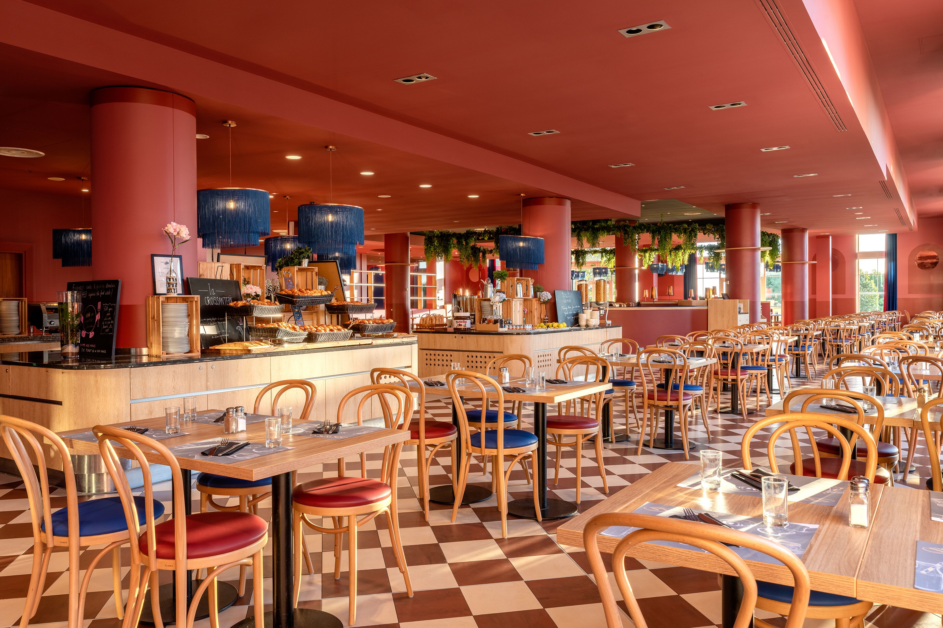 Een ruime restaurantruimte met zwart-wit geruite vloer, houten tafels en stoelen, en een bar in het midden.