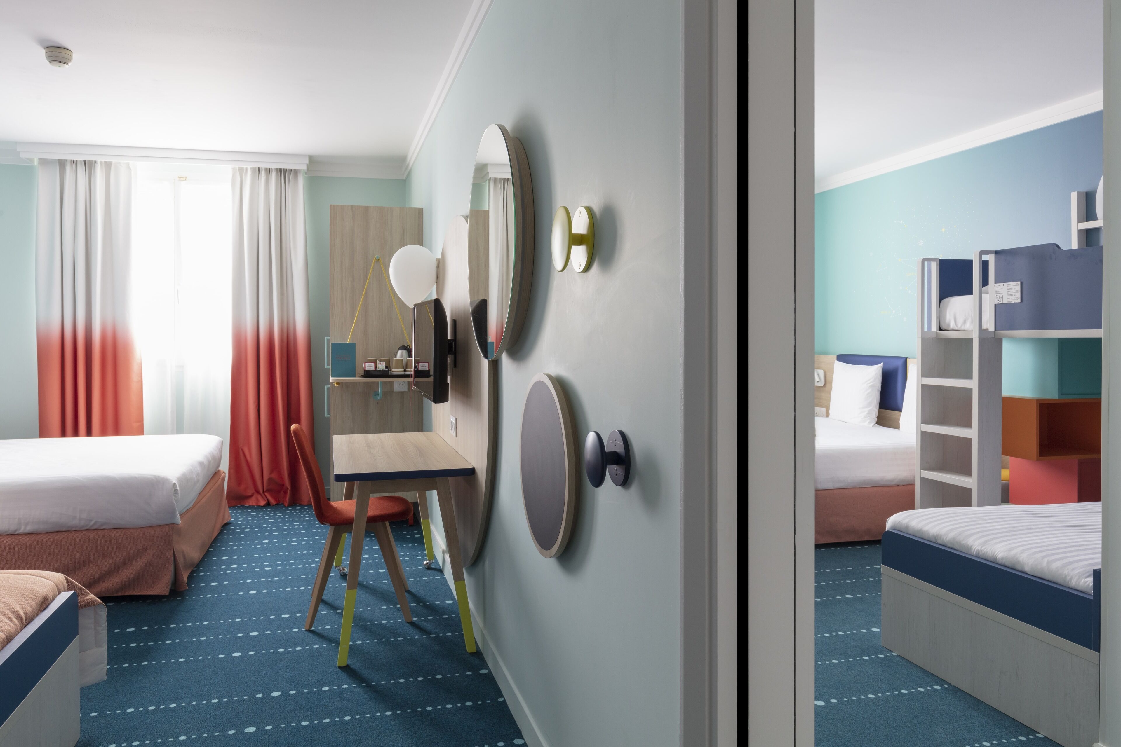 A hotel room with two beds, a desk, a chair, and a mirror.