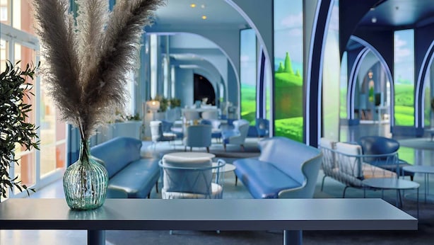 Un moderno vestíbulo de hotel con una zona de estar curva, un ventanal con vistas a la vegetación y un jarrón decorativo con plumas de pampa.