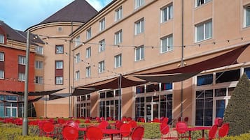 Et hotels ydre med udendørs siddepladser og store vinduer.