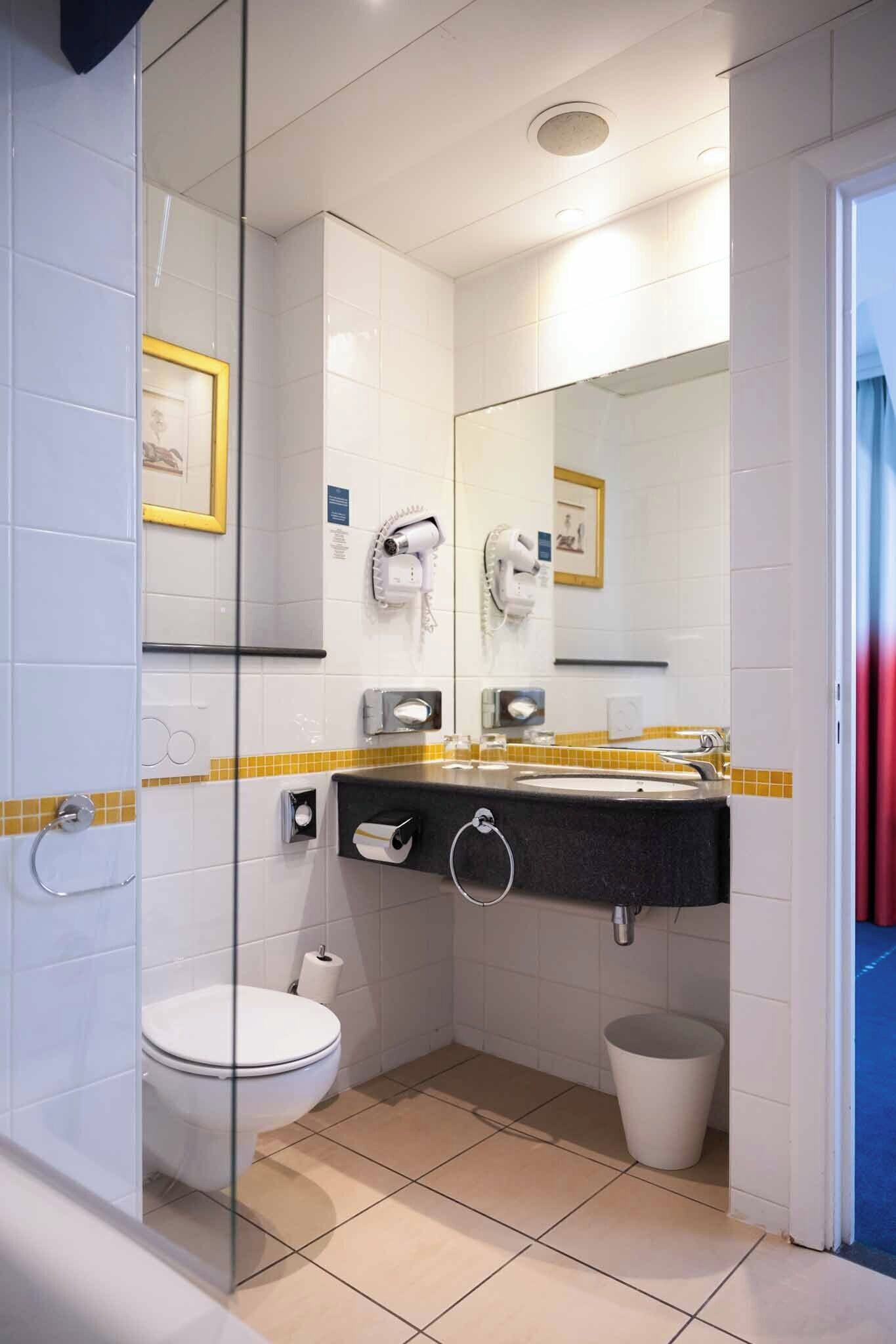 A modern bathroom with a glass partition, a white toilet, a sink with a towel ring, and a hand dryer.