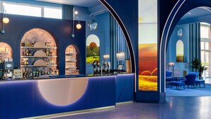 Un área de bar moderna con una barra curva, estantes con botellas y un gran mural de un atardecer.