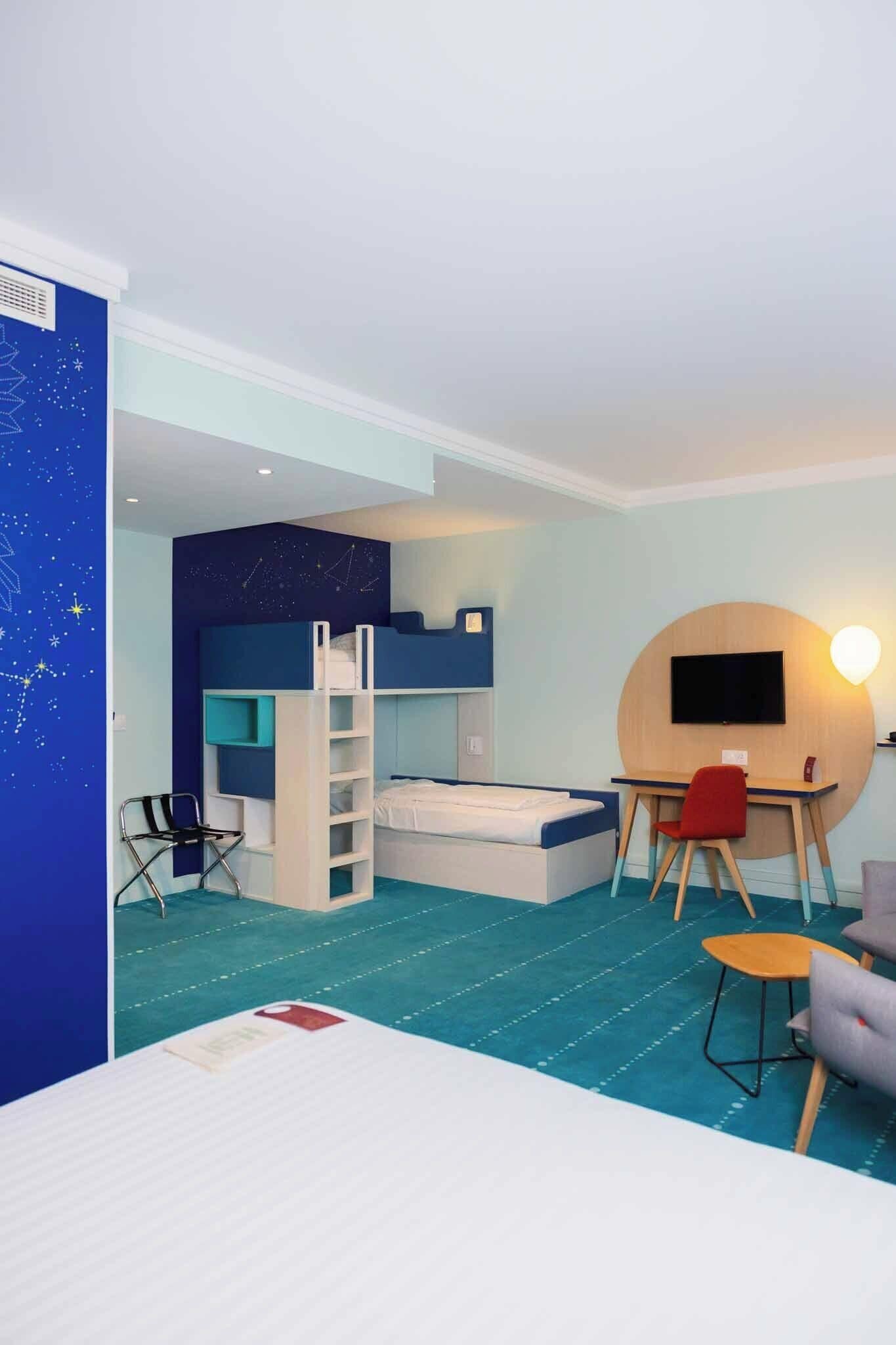 Une chambre avec des lits superposés, un bureau, une chaise et un téléviseur.