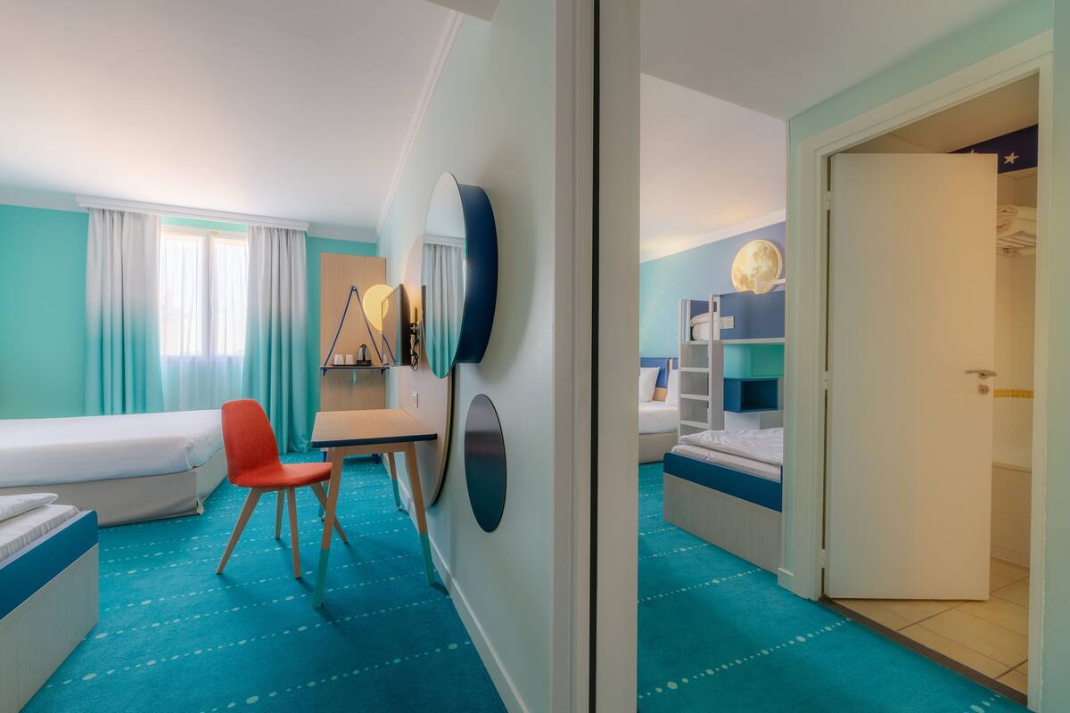 A hotel room with a bed, a desk, a chair, a TV, and a wardrobe.