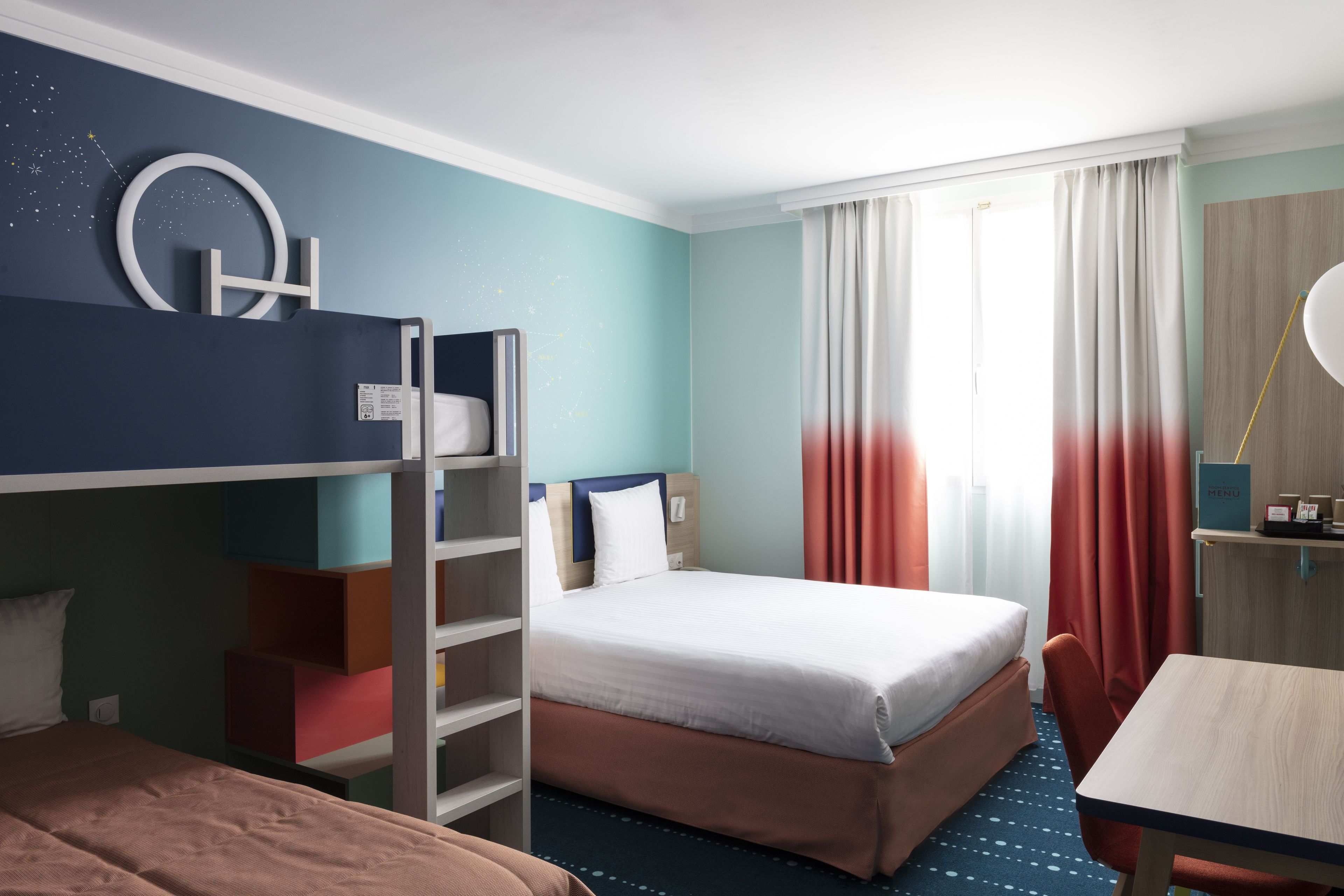 Una habitación de hotel con una cama nido, una cama individual, un escritorio y una silla.