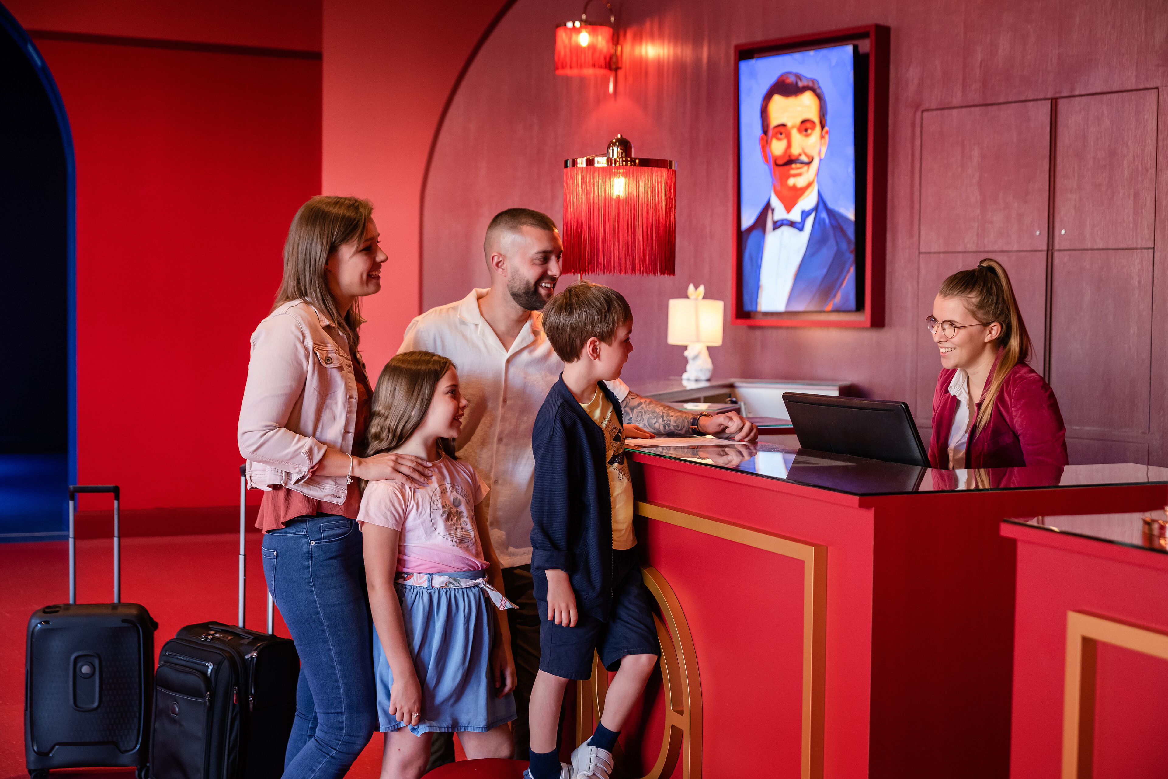 Una familia en la recepción de un hotel, con un televisor mostrando a un hombre con traje.