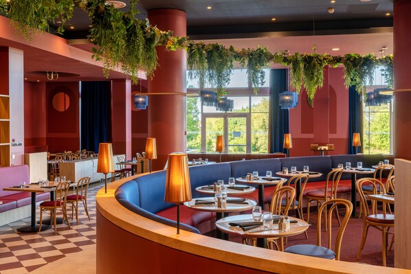 Un restaurant avec des tables rondes, des sièges confortables et des plantes suspendues.