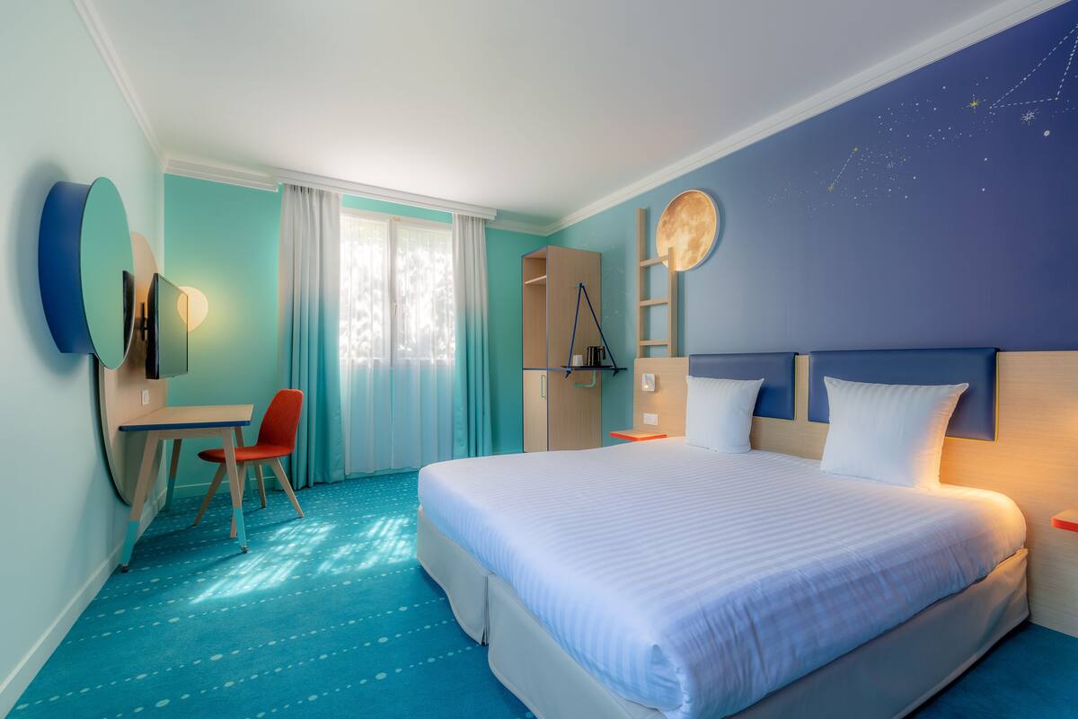 A hotel room with a large bed, a desk, a chair, and a wardrobe.