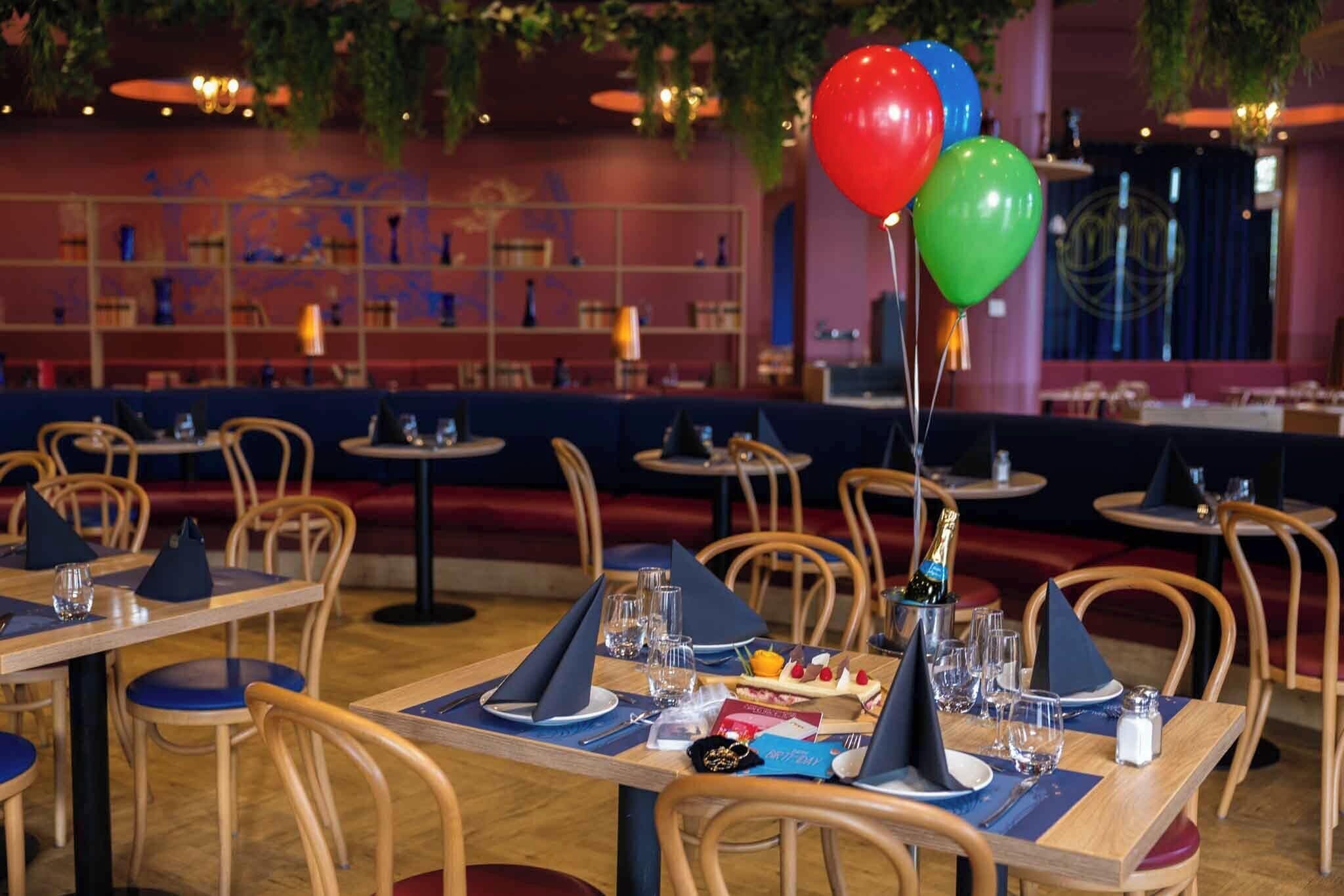 Un restaurant avec des tables en bois, des serviettes bleues et des ballons.