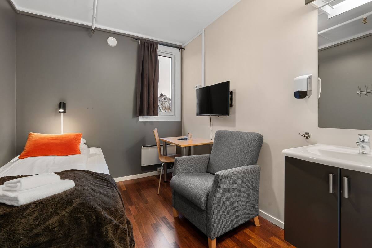 Una habitación de hotel moderna con una cama, una silla, un escritorio, un televisor y un baño.