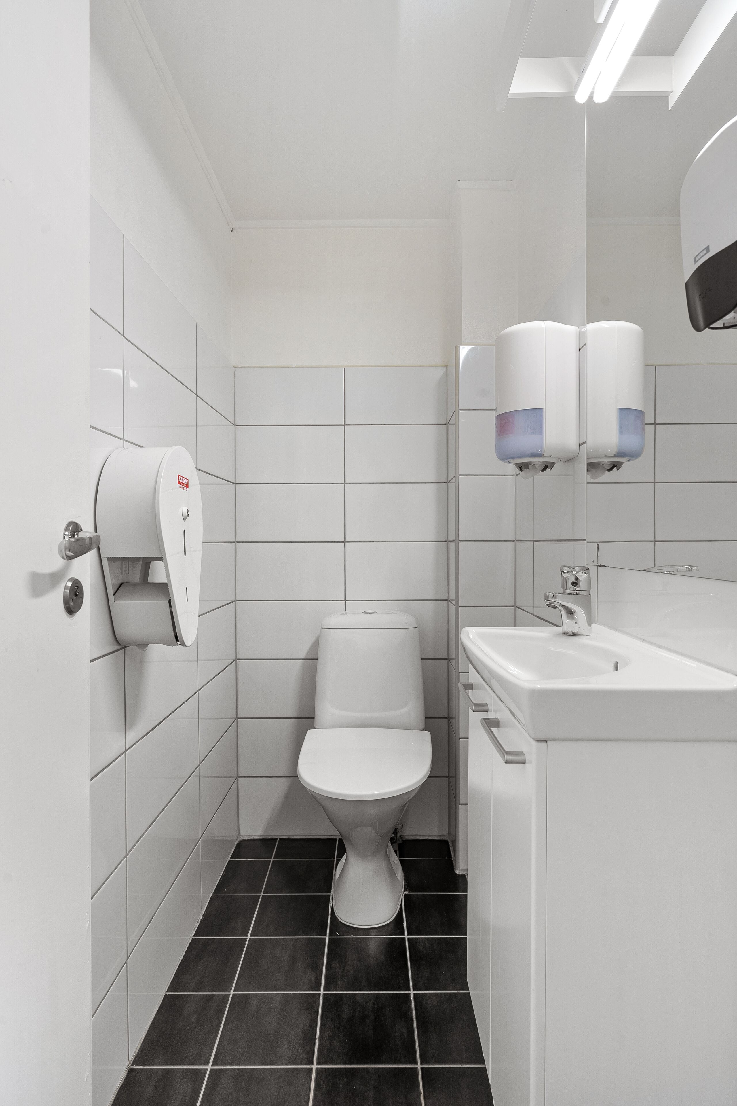 A modern bathroom with a toilet, sink, and hand dryer.