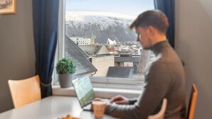 Una persona trabajando en un escritorio junto a una ventana con vista a un paisaje urbano y una montaña.