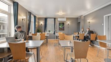 A modern dining area with wooden tables and chairs, a staircase, and a view of the city.