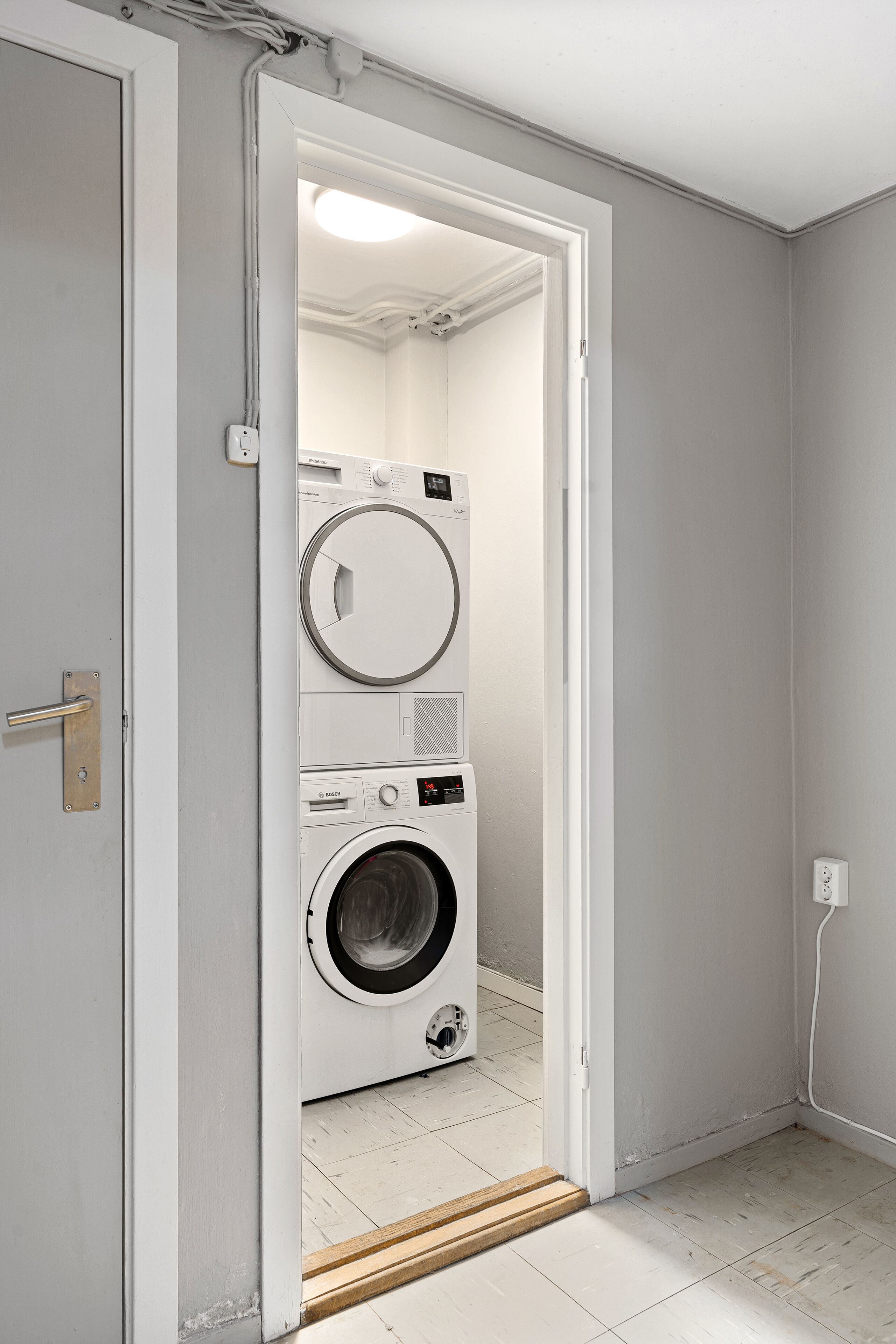 A laundry room with a front-loading washer and dryer, a wooden door frame, and a white tiled floor.