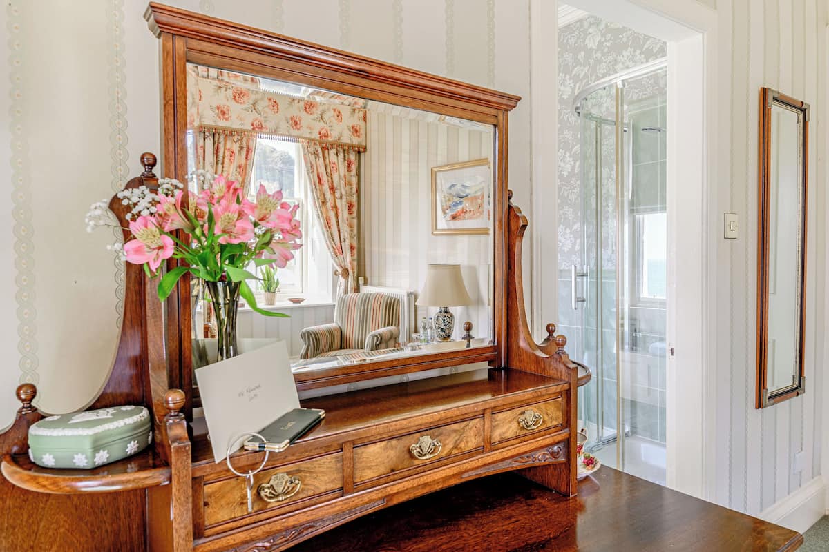 A wooden vanity with a large mirror, a vase of flowers, and a framed picture on the dresser.