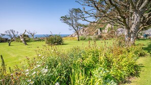 Un exuberante jardín con diversas plantas y árboles, un cielo azul despejado y una vista del mar al fondo.