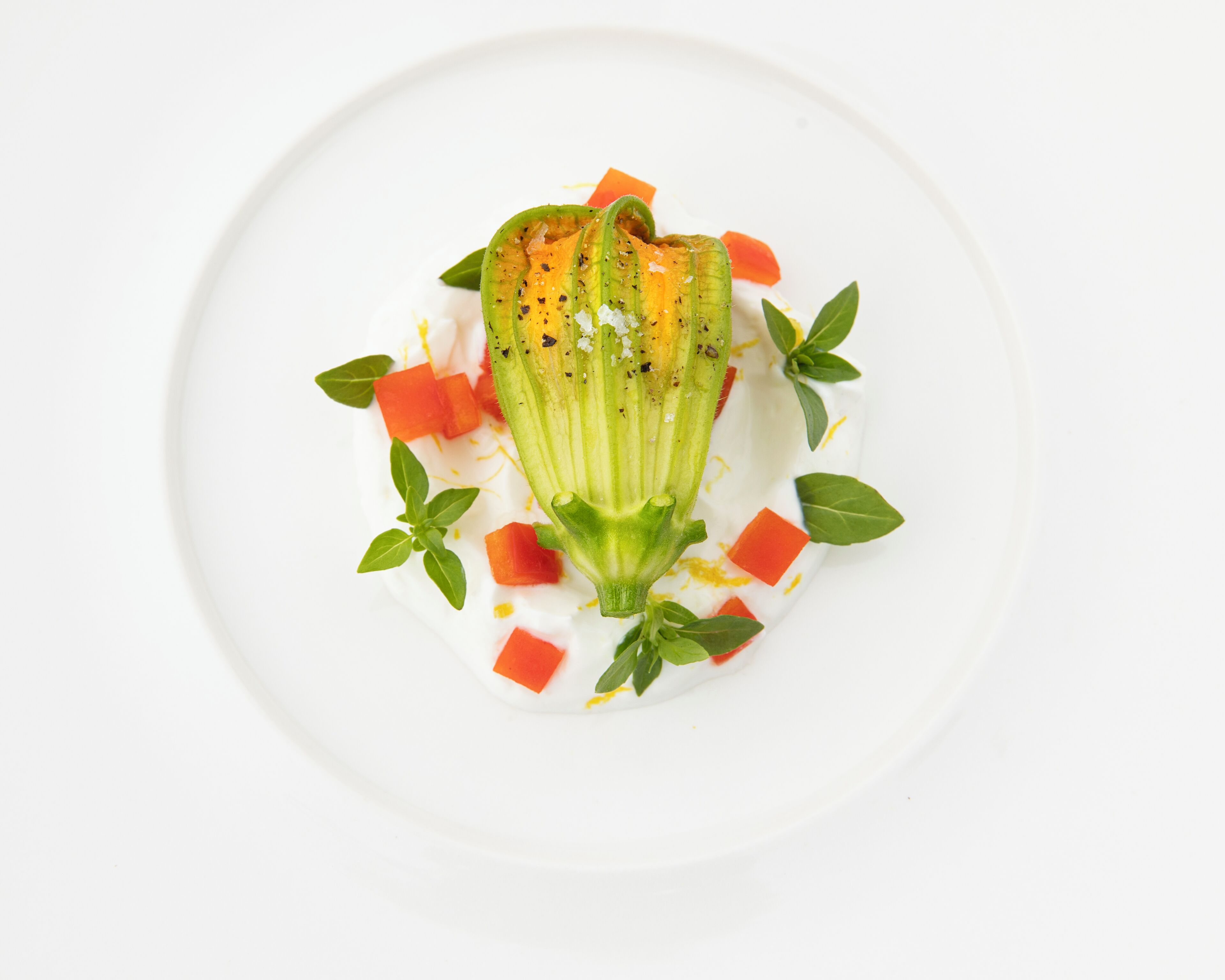 A white plate with a dish featuring a green vegetable, possibly okra, with red cubes and green leaves.