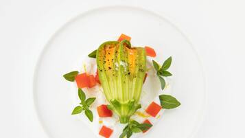A white plate with a dish featuring a green vegetable, possibly okra, with red cubes and green leaves.