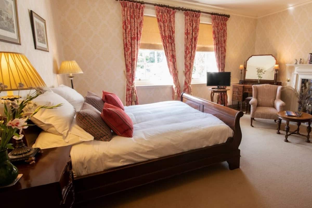 A well-appointed bedroom with a large bed, a sitting area with a chair and a small table, a television, and a fireplace.