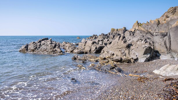 Una costa rocosa con aguas azul cristalinas y una playa de guijarros.