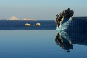 A clear view of a swimming pool with a rock formation on the right and distant islands in the background. - Vrahos Boutique Hotel (Folegandros)