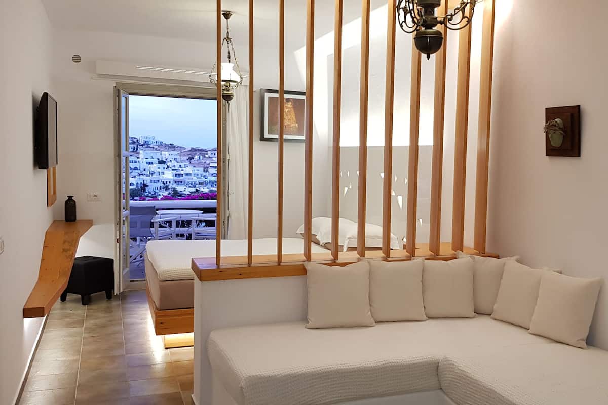 Un dormitorio moderno con una cama grande, un panel divisor de madera, vistas a un pueblo costero y una ventana con vista al mar.