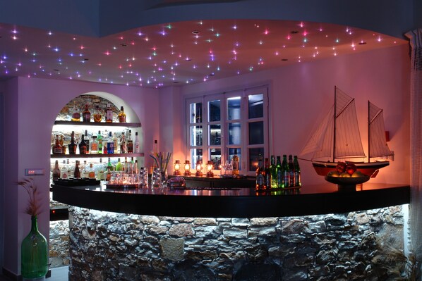 Zona de bar con pared de piedra, decoración náutica y estante con botellas.