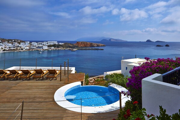 A pool area with lounge chairs and a view of the sea and buildings. - Vrahos Boutique Hotel (Folegandros)