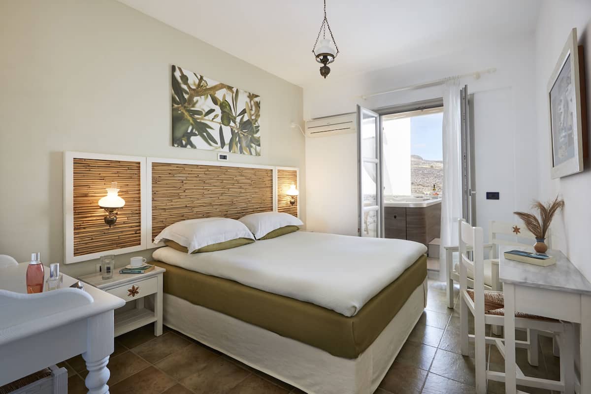 Un dormitorio con cama, mesitas de noche, un escritorio y vistas al exterior.