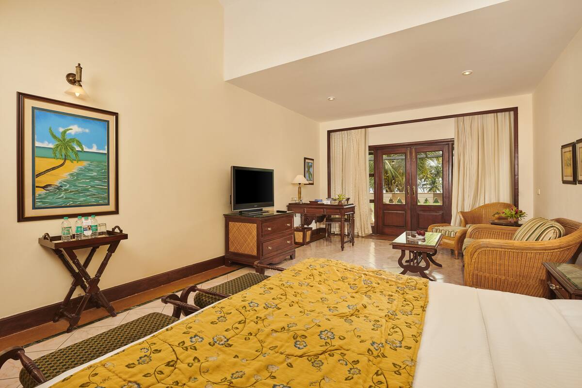 A hotel room with a bed, a desk, a television, a wicker chair, and a painting of a beach scene.