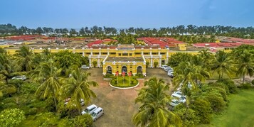 Un edificio grande de color amarillo con techo rojo, rodeado de palmeras y coches estacionados.