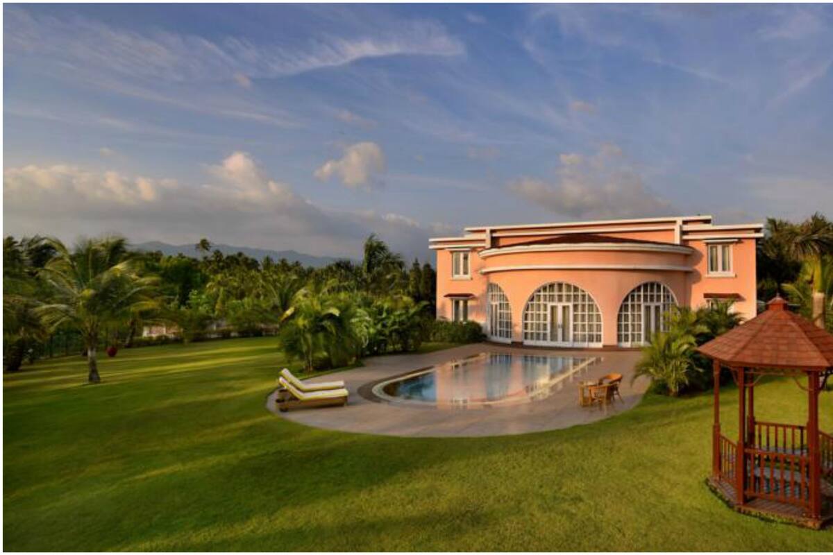 A large building with a swimming pool, surrounded by lush greenery and palm trees.