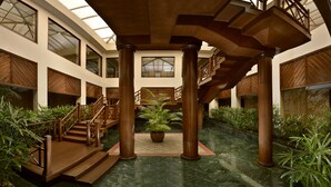 A spacious atrium with a central staircase, wooden columns, and potted plants.