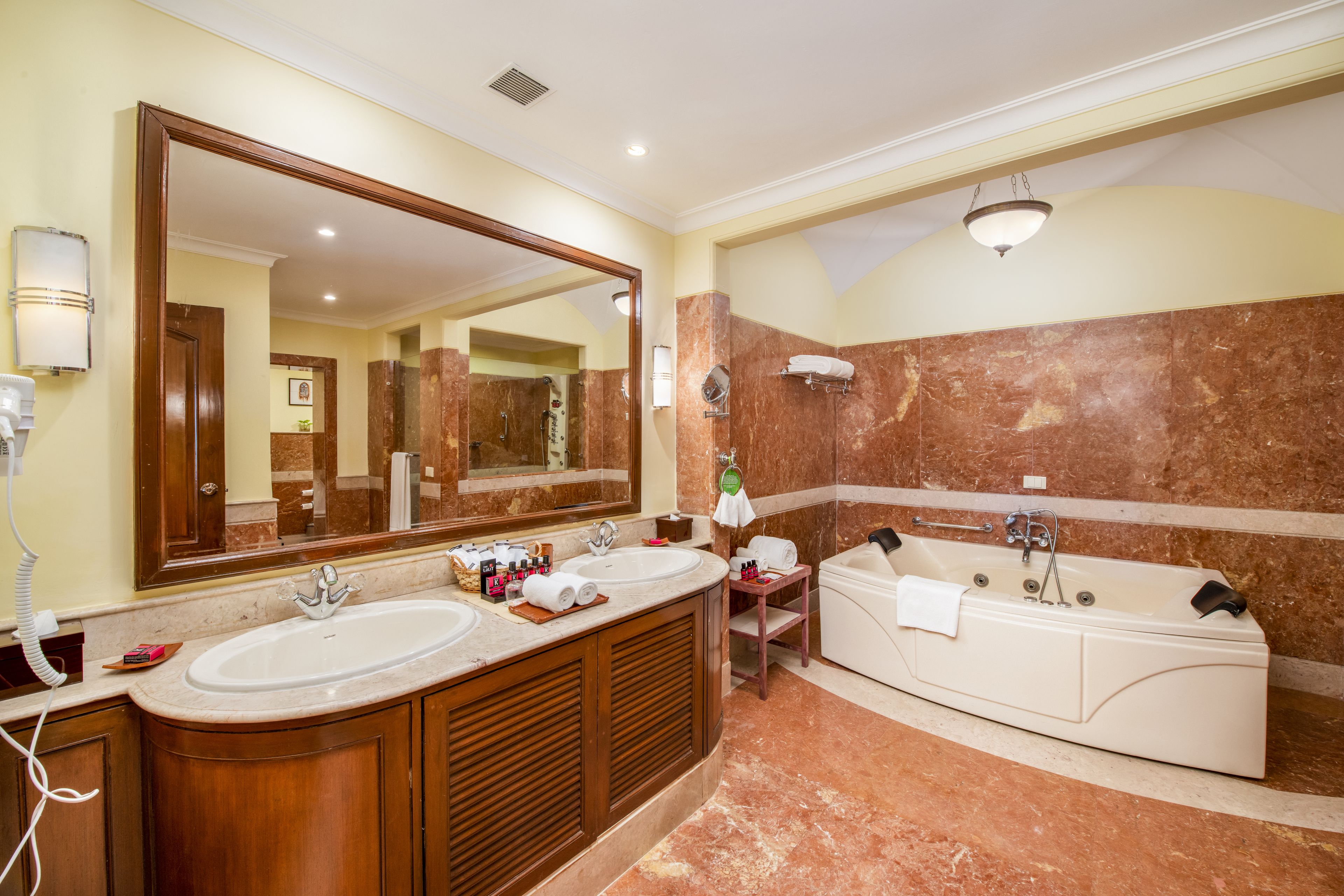 Un baño con dos lavamanos, un espejo grande, una bañera y un mueble de tocador con un perchero para toallas.
