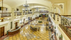 A spacious lobby with high ceilings, chandeliers, and a tiled floor.