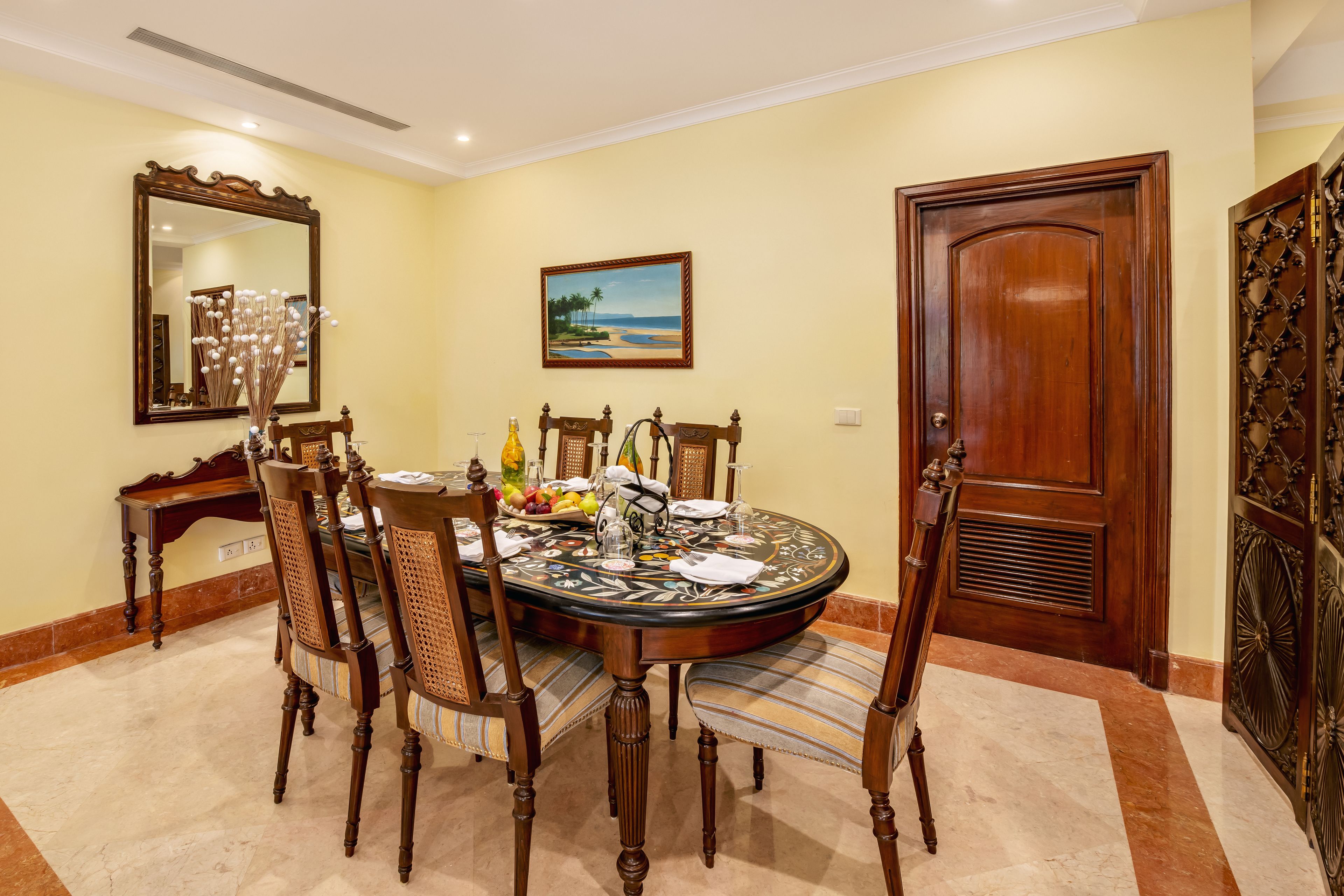 Un comedor con una mesa redonda, seis sillas, un cuadro, un espejo y una puerta de madera.
