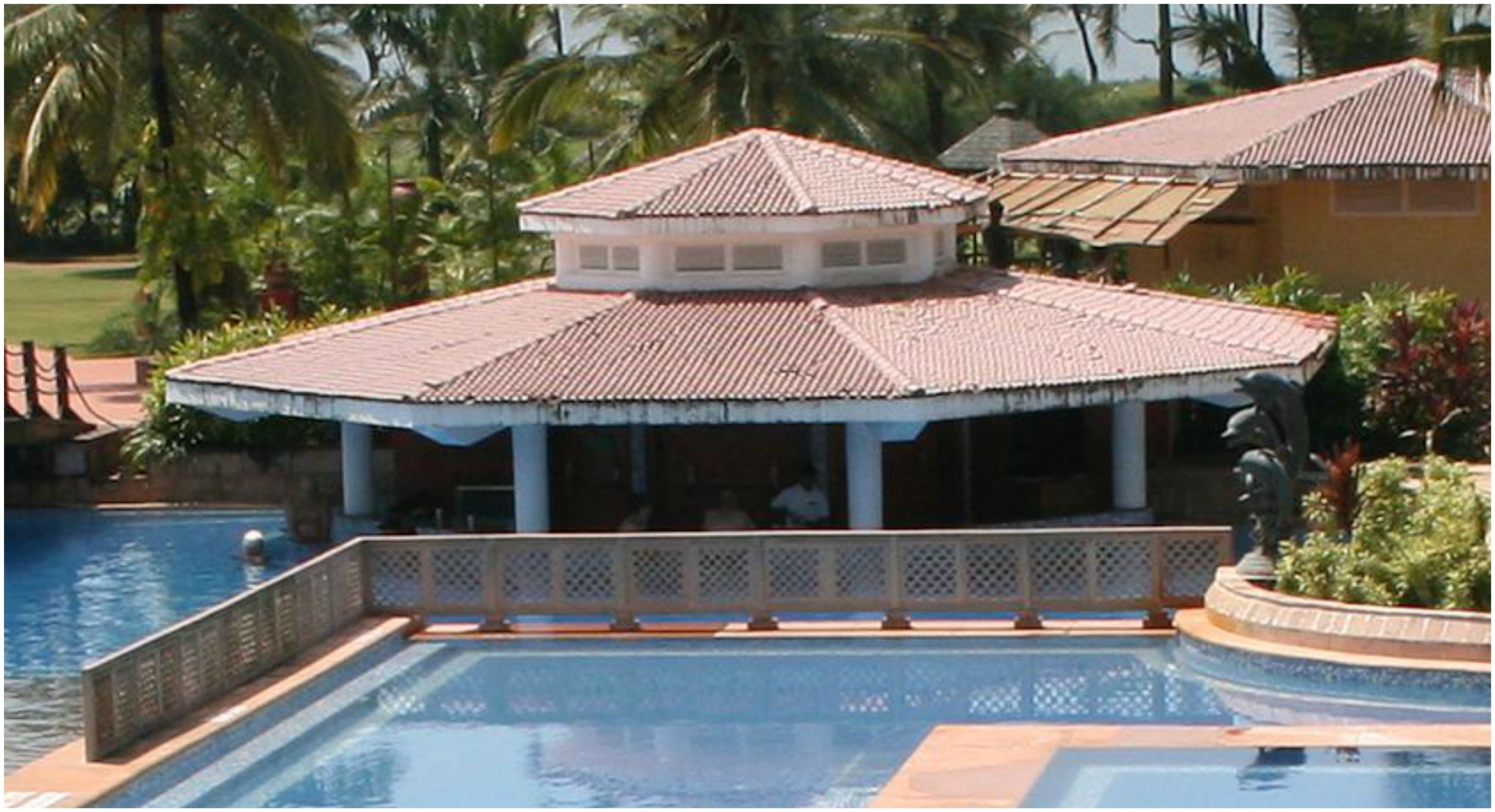 A poolside area with a covered seating area, a swimming pool, and a building with a tiled roof.