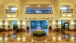 A spacious lobby with a tiled floor, a central fountain, and a view of a tropical garden through a large window.