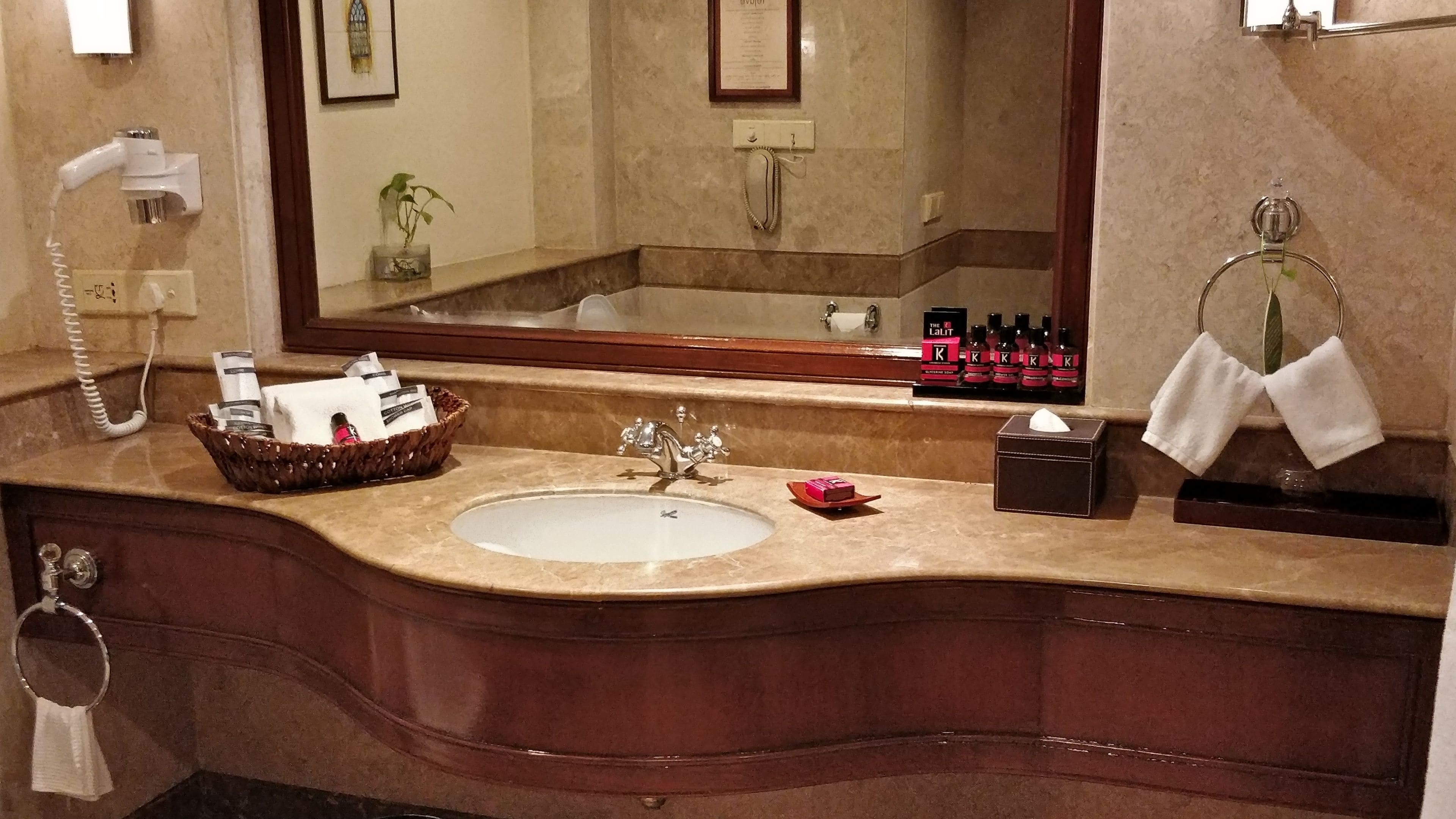 A bathroom with a marble sink, a mirror, a telephone, a basket with toiletries, and a towel rack.