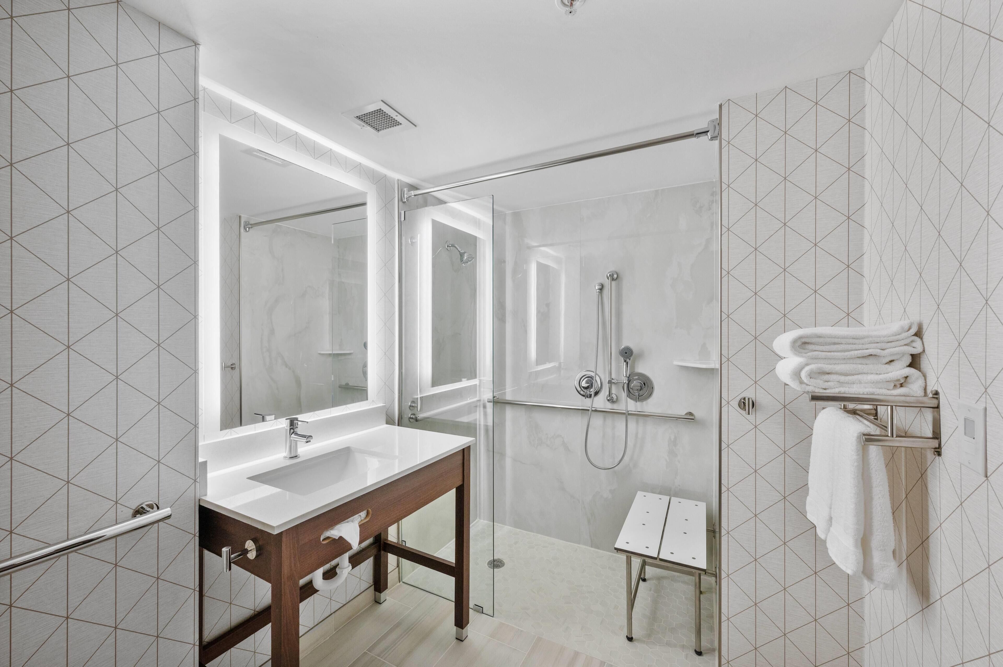 A modern bathroom with a glass shower enclosure, a sink with a mirror, and a towel rack.