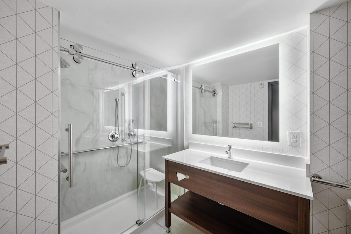 A modern bathroom with a glass-enclosed shower, a large mirror, and a white vanity.