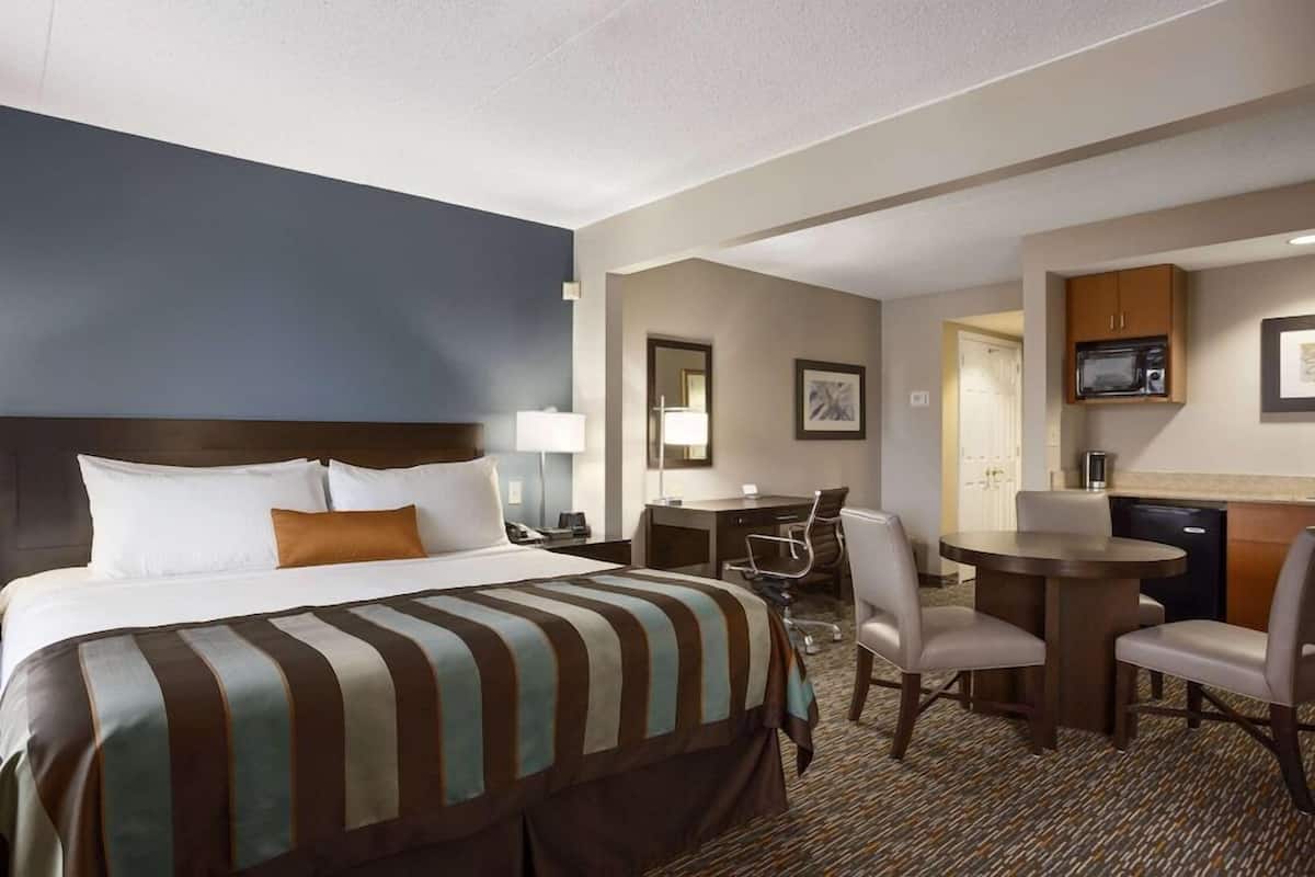 A hotel room with a large bed, a desk, a chair, a microwave, and a small kitchenette.