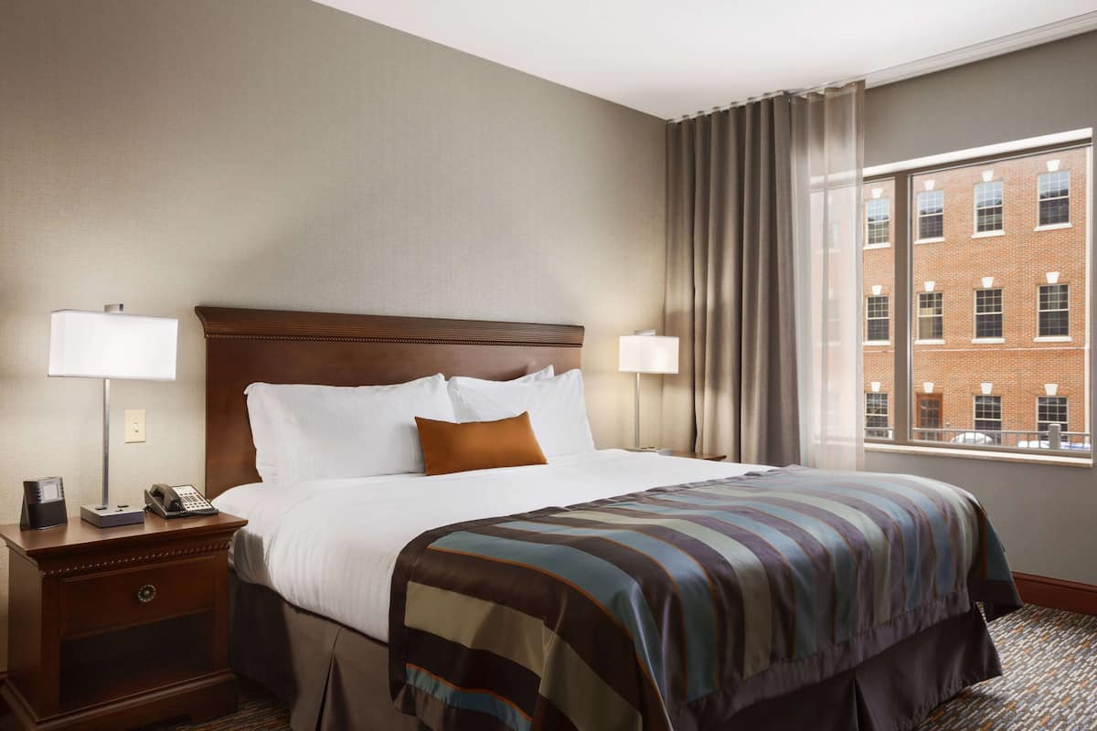A hotel room with a large bed, two bedside tables with lamps, a telephone, and a window with a view of a brick building.