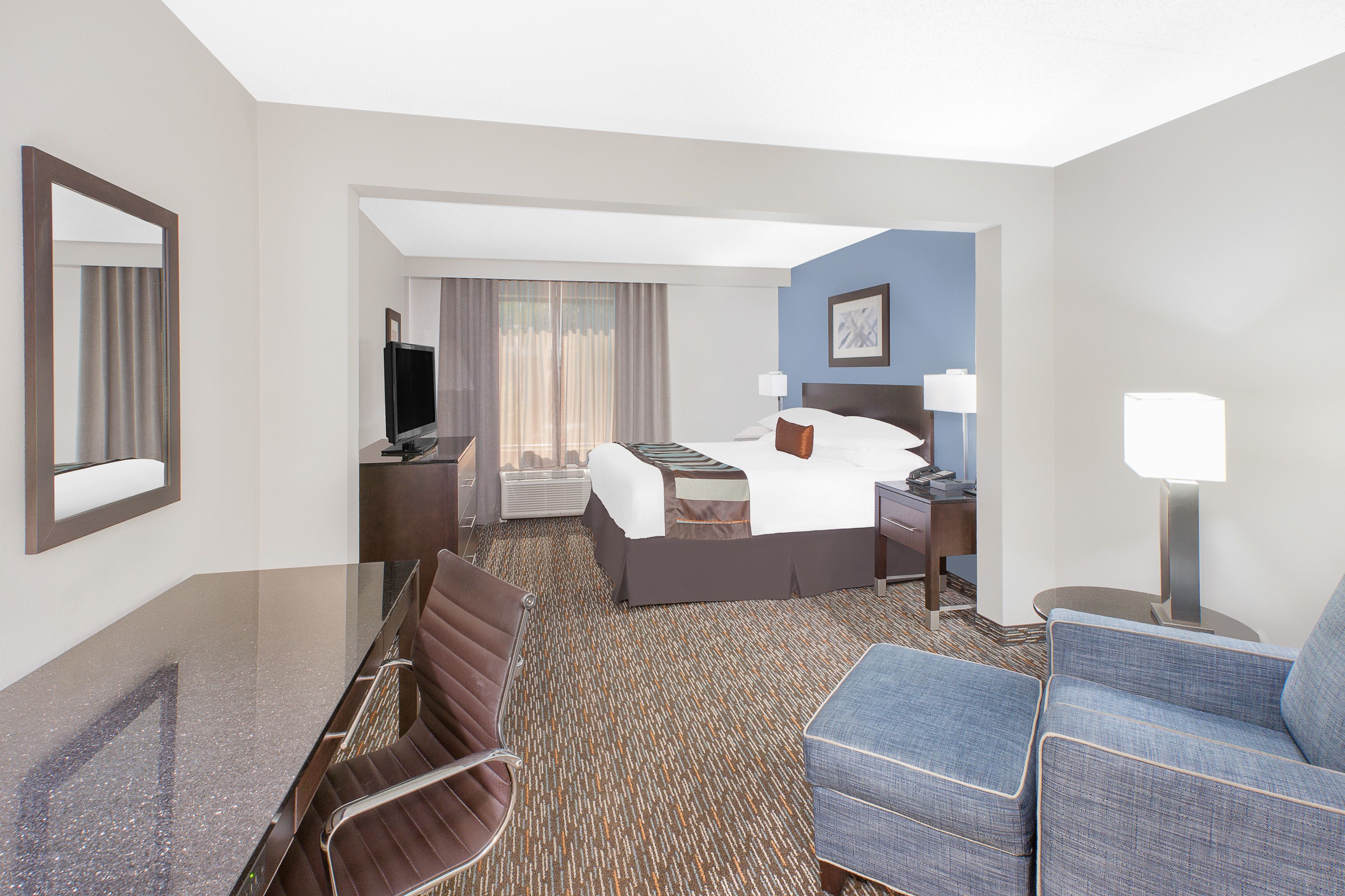 A hotel room with a bed, a desk, a chair, a television, and a lamp.
