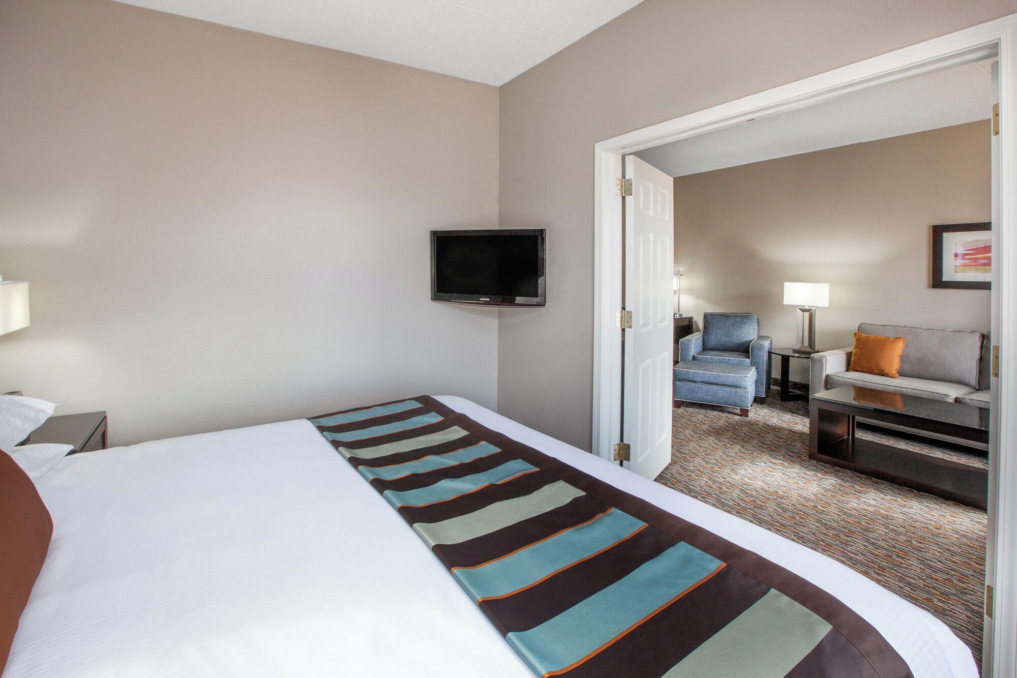 A hotel room with a bed, a television mounted on the wall, a sofa, and a chair.